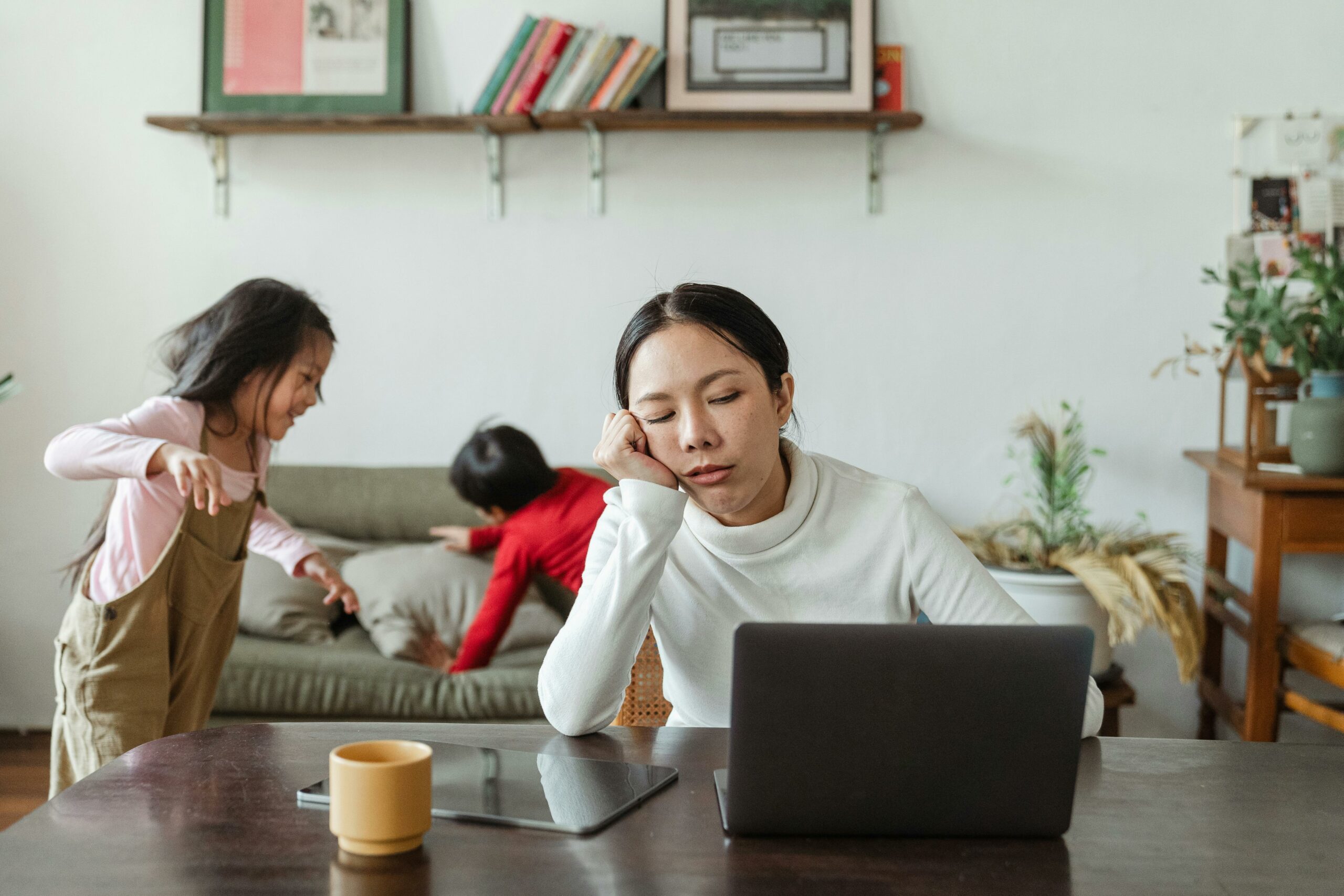 Tired woman on a laptop with her kids playing in the background